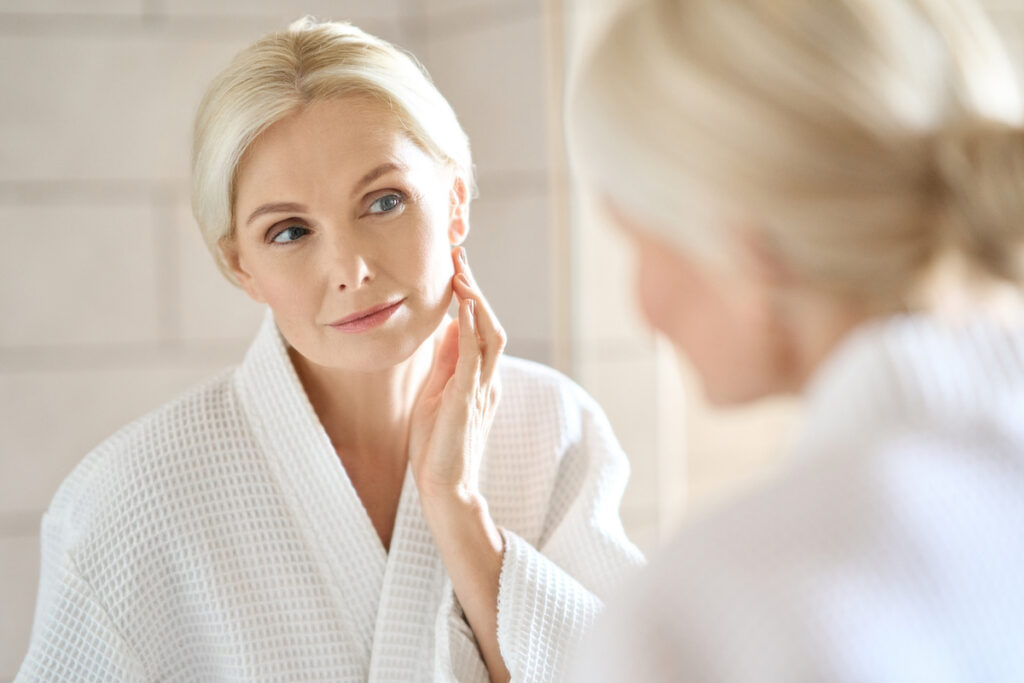 Senior Woman Wearing Robe Looks in Mirror_Natural Aging