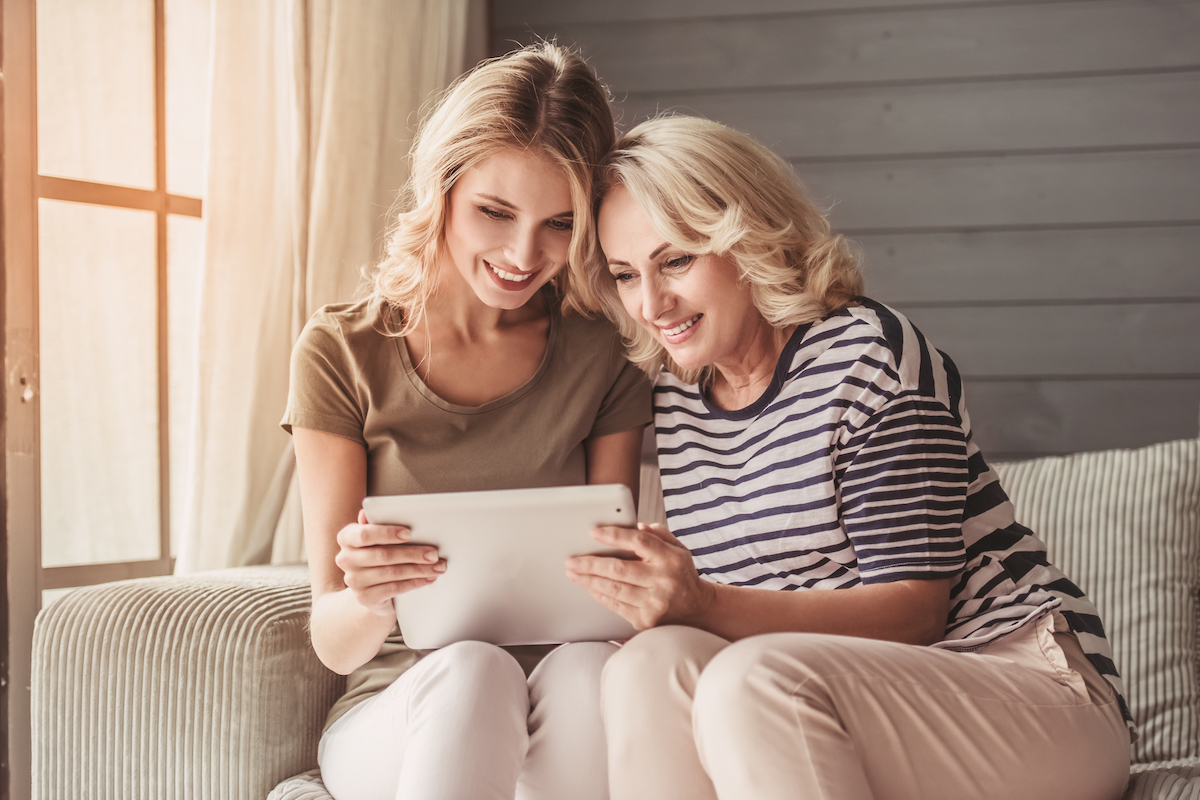Senior Woman and Adult Daughter Sit on Couch and Look at Tablet_Senior Living Communities