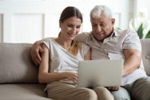 Senior Man and Adult Daughter on Couch Looking at Laptop_Memory Care