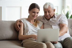Senior Man and Adult Daughter on Couch Looking at Laptop
