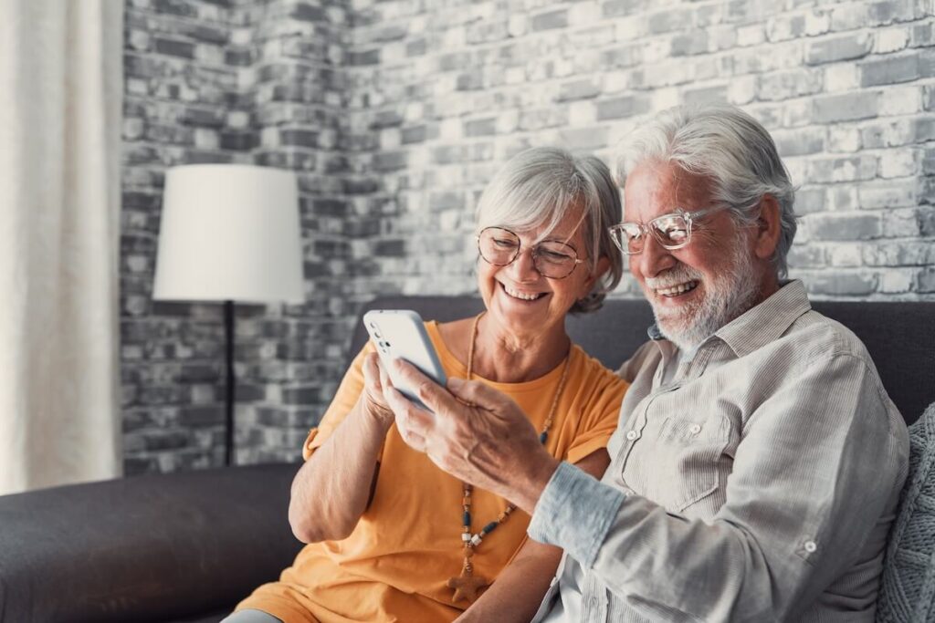 Senior Couple Smiling at Phone While Sitting on Couch